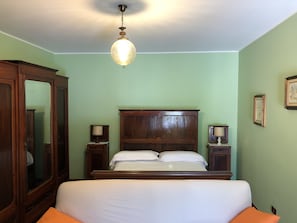 Un dormitorio con una cama de madera, dos mesitas de noche con lámparas, un espejo grande y una lámpara colgante.