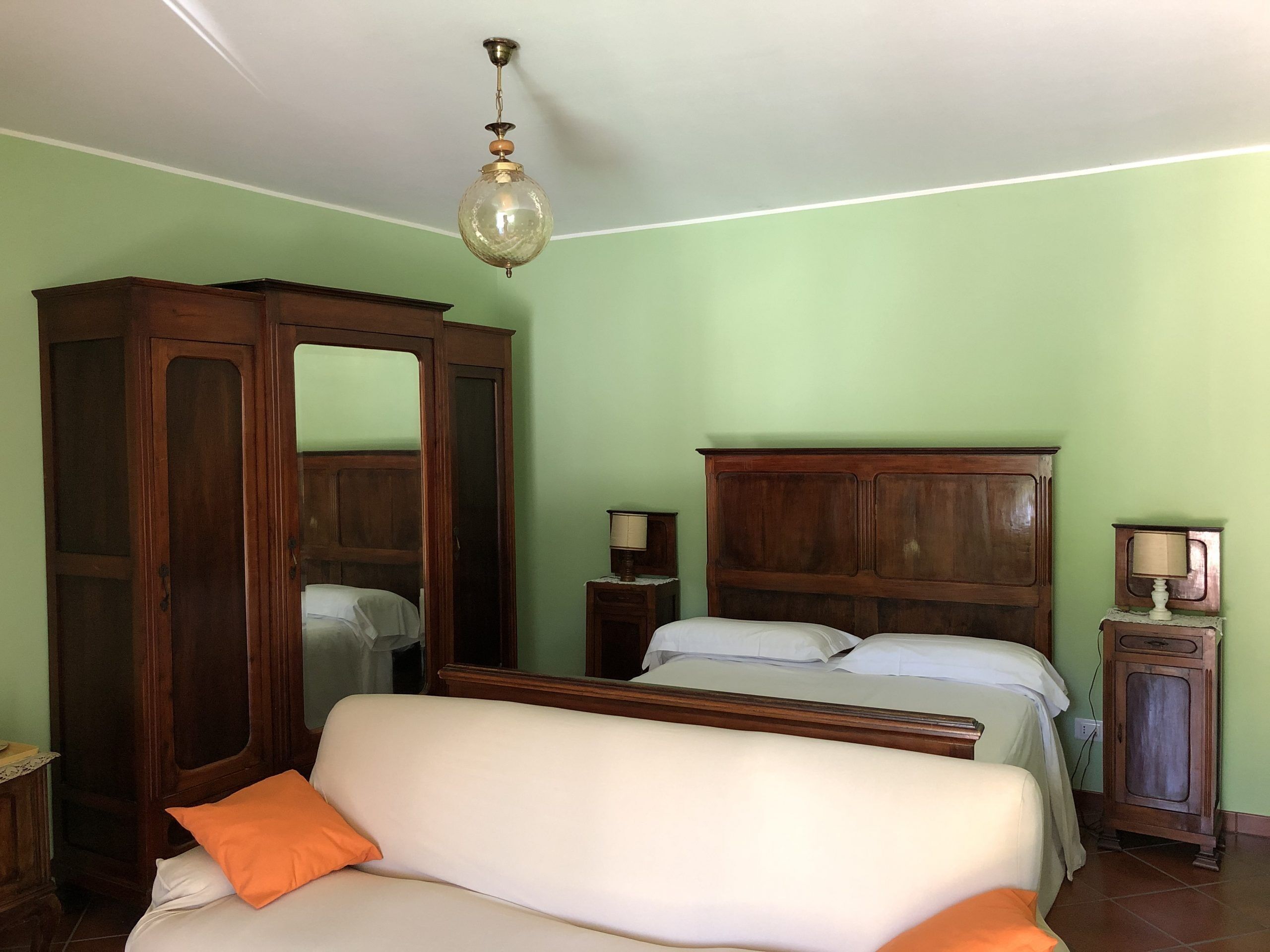 A bedroom with a bed, a wooden wardrobe, a mirror, and a ceiling fan.