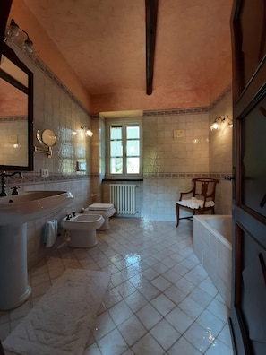 Un baño con un lavamanos grande, dos inodoros, una bañera y una ventana.