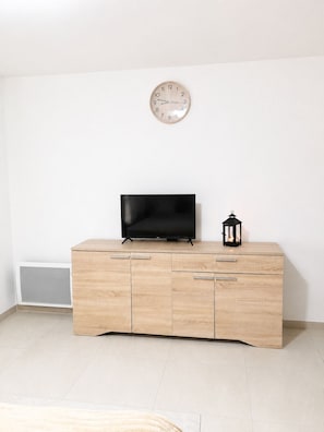 Una habitación con un armario de madera, un televisor negro, un reloj de pared y un pequeño farol negro.