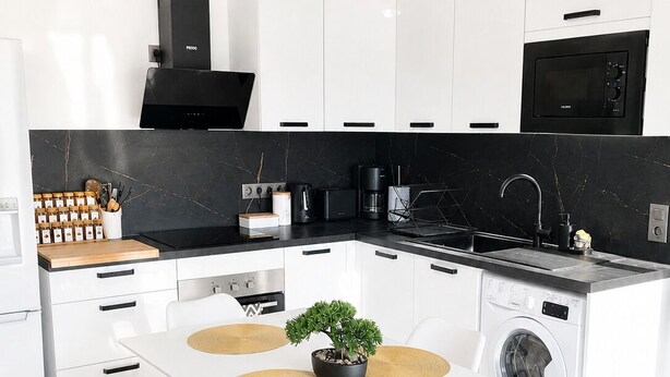 Una cucina moderna con mobili bianchi, un piano di lavoro nero, forno a incasso, microonde e lavatrice.