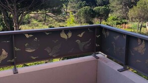 Un balcone con ringhiera in metallo decorata con sagome di uccelli, pavimento piastrellato e vista su un paesaggio verdeggiante con alberi.
