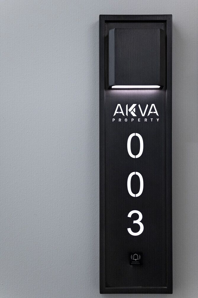 Un écran numérique noir affiche les mots « AKVA PROPERTY » et le chiffre « 003 » sur un mur.