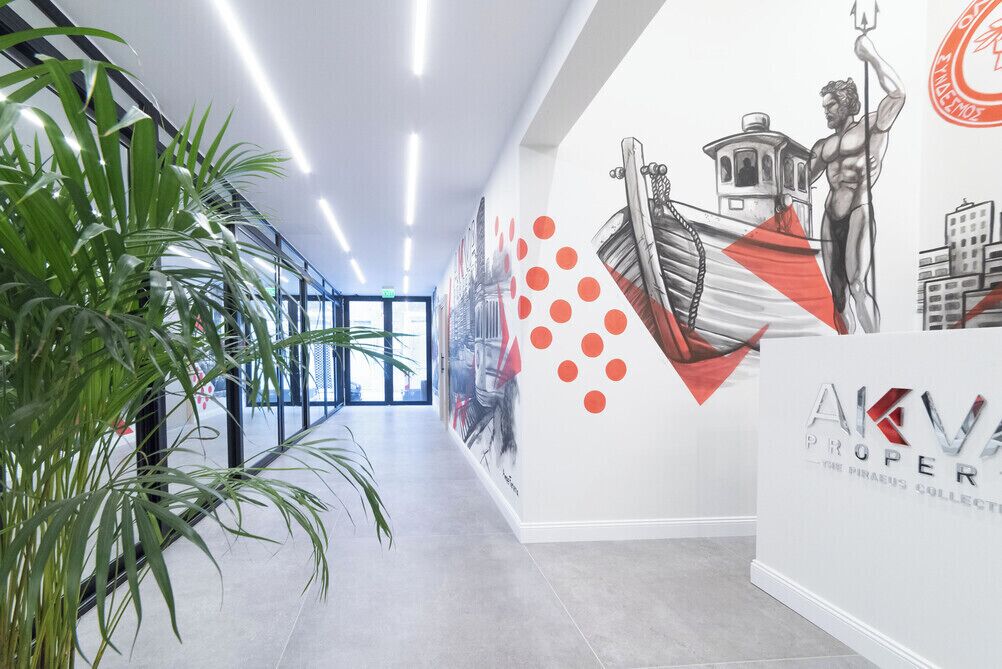 Un pasillo de diseño moderno, con un mural que muestra un barco y una estatua, y un cartel que dice 'AKV PROPER'.