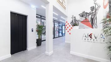 Un interior moderno con un ascensor negro, una planta en maceta y una pared con un logo y obras de arte.