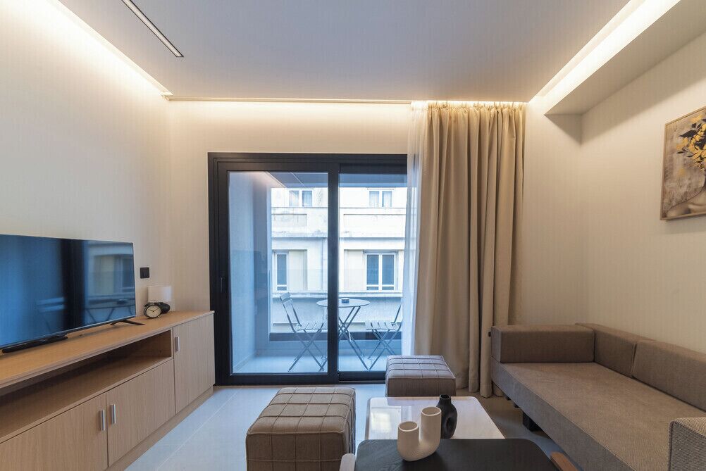 Una sala de estar moderna con un televisor de pantalla plana, un sofá, una mesa de centro y un balcón con una mesa y sillas.