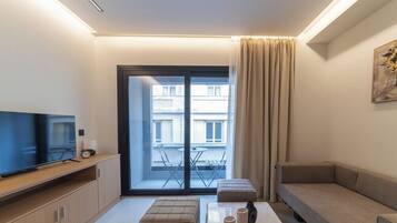 Una sala de estar moderna con un televisor de pantalla plana, un sofá, una mesa de centro y un balcón con una mesa y sillas.