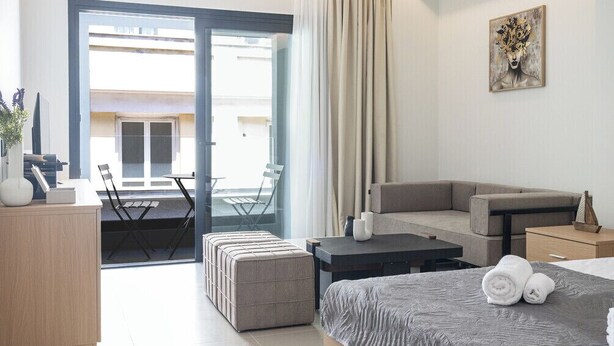 Una habitación de hotel moderna con cama, sofá, mesa de comedor, escritorio pequeño, silla y balcón con vistas.