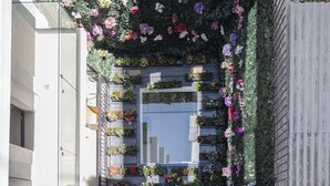 Un edificio con fachada de vidrio reflectante, varias terrazas con jardineras y barandilla de metal.