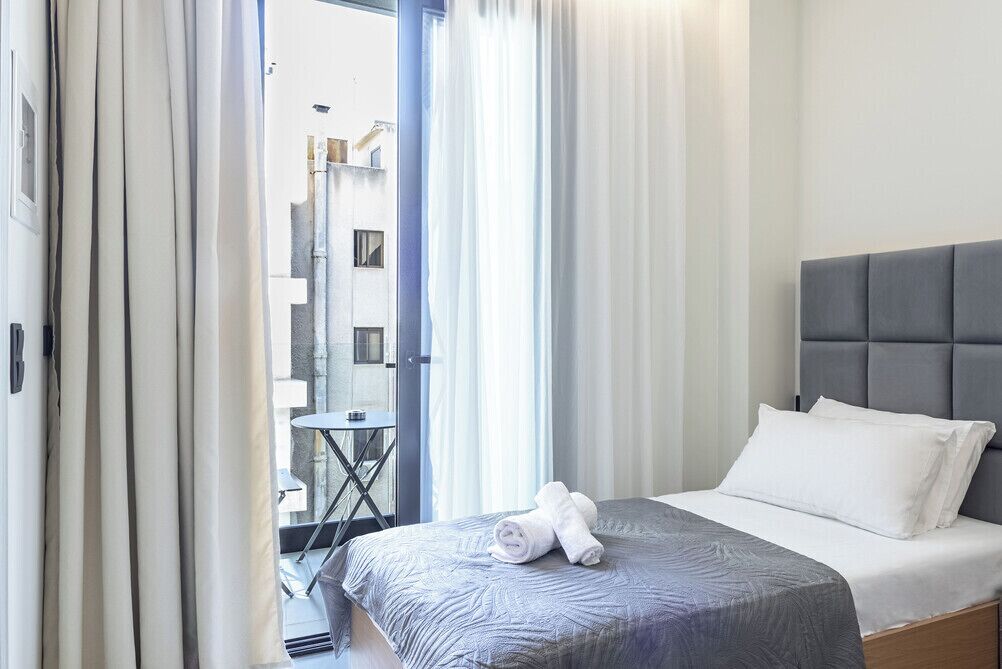 A hotel room with a bed, a small table, and a view of the outside.