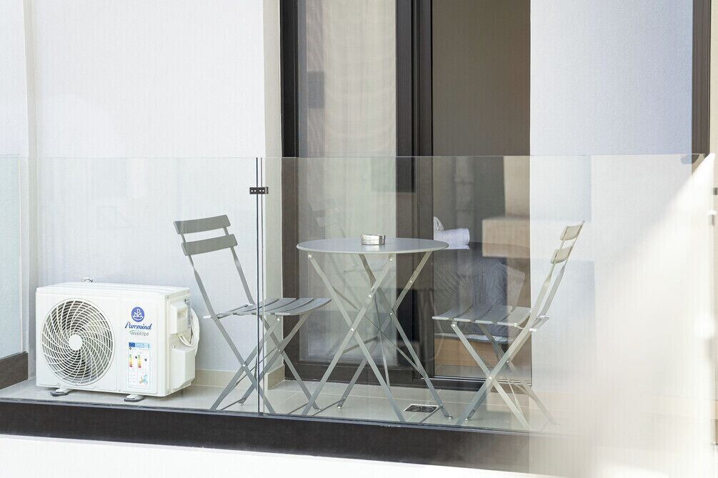 A balcony with a glass partition, a table, two chairs, and an air conditioning unit.