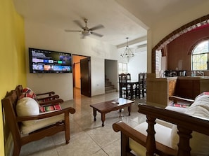 A living room with a TV, wooden furniture, a ceiling fan, and a staircase leading to another level. - Modern Mexican-Style House Just Steps from the Stadium and Close to the Beach and the Boardwalk ⭐ (Puerto Vallarta)