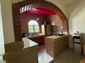 Una cocina compacta con un arco de ladrillo, una ventana, un fregadero, una estufa y un refrigerador.