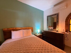A bedroom with a bed, nightstand, dresser, mirror, and an arched window. - Modern Mexican-Style House Just Steps from the Stadium and Close to the Beach and the Boardwalk ⭐ (Puerto Vallarta)