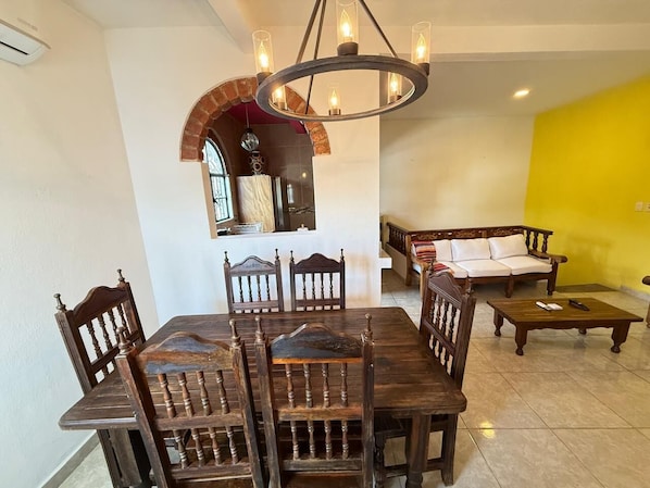 Un comedor con una mesa y sillas de madera, una araña y un sofá al fondo.