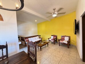 Un salon avec un mur jaune, un ventilateur de plafond et une table basse en bois.