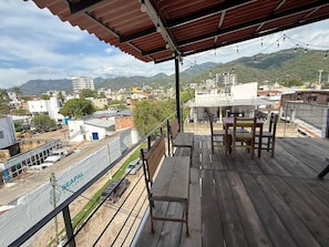 Una terraza de madera con una mesa y sillas, con vistas a un paisaje urbano con edificios y montañas.