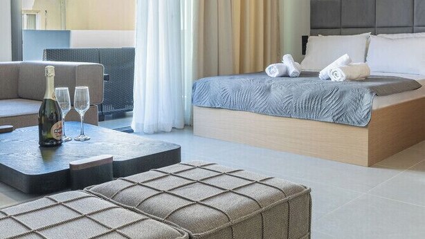 Ett modernt hotellrum med en säng, en sittgrupp med en flaska och glas, och utsikt genom ett fönster.
