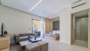 Ett modernt hotellrum med en soffa, en säng, ett skrivbord med en dator och en glasdörr som leder till badrummet.
