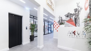 A modern interior with a black elevator, a potted plant, and a wall with a logo and artwork. - Bright Retreat in Piraeus | Feel Right at Home (Athens)