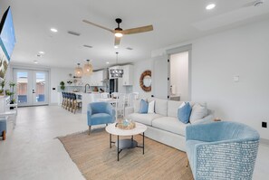 Ein modernes Wohnzimmer mit einer Couch, Sesseln, einem Essbereich und einer Küche im Hintergrund.