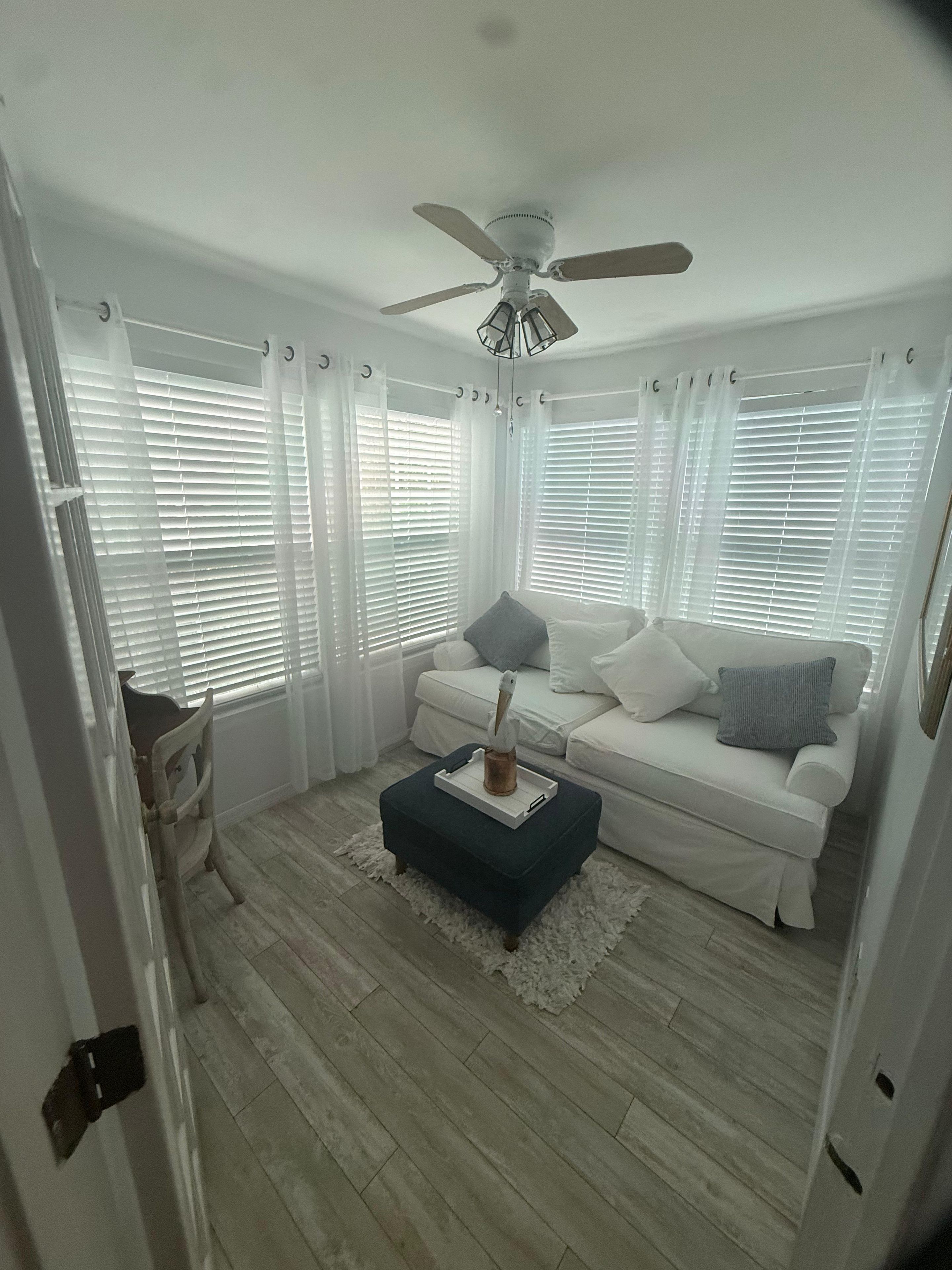 A living room with a white sofa, a blue ottoman, and a ceiling fan.