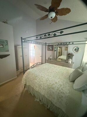 Ein Schlafzimmer mit einem Himmelbett, einem Deckenventilator, einem Spiegel und einer Tür zu einem anderen Raum.
