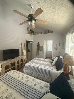 Ein Schlafzimmer mit einem Bett, einem Fernseher, einem Deckenventilator und einem Fenster mit Jalousien.