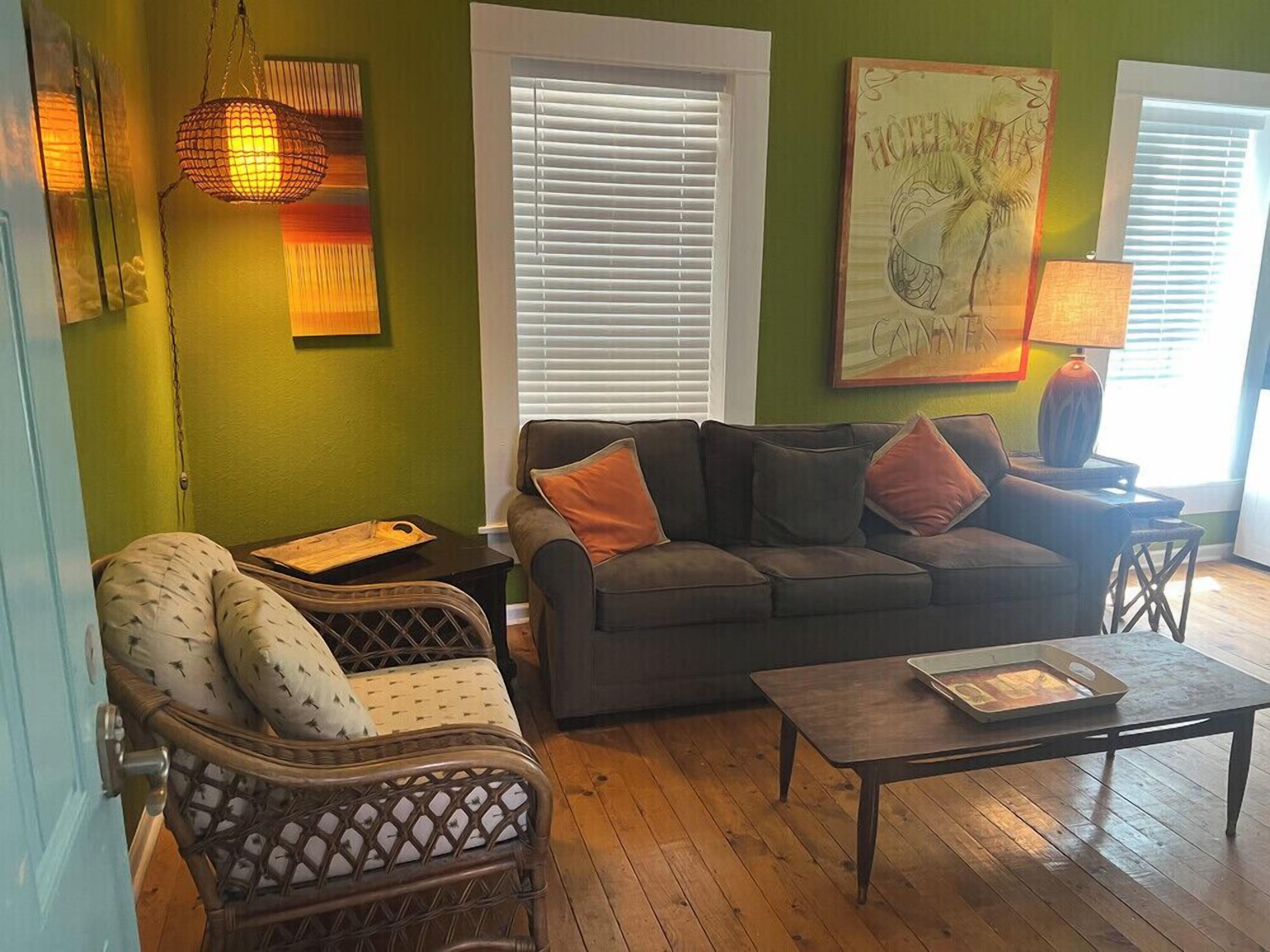 A living room with a sofa, armchair, and coffee table. There is a painting on the wall and a lamp on a side table.
