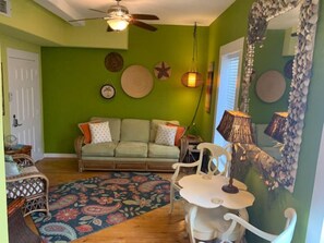 Ein Zimmer mit grüner Wand, einer Couch, einem gemusterten Teppich, einem Deckenventilator und einem Tisch mit Stühlen.