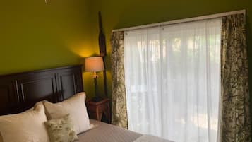 A bed with pillows, a nightstand with a lamp, and a window with sheer curtains.