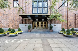 A brick building with a central entrance, potted plants, and a tiled ground.