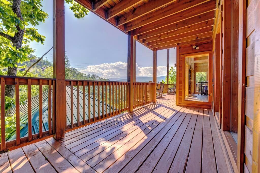 Une terrasse en bois avec une rambarde, une porte donnant sur l’intérieur et une vue sur les arbres et les montagnes en arrière-plan.