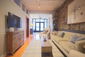 Ein Wohnzimmer mit Sofa, Couchtisch, Fernseher, Holzschrank und einer Ziegelwand mit einem gerahmten Bild.