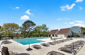Ein Swimmingpool mit Liegestühlen, ein Gebäude mit rotem Dach und Bäume im Hintergrund.