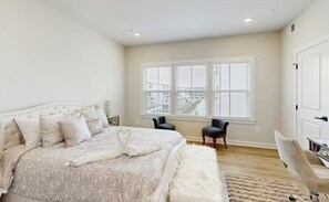 Ein Schlafzimmer mit einem großen Bett, zwei Stühlen, einer weißen Tür und einem Fenster mit Jalousien.