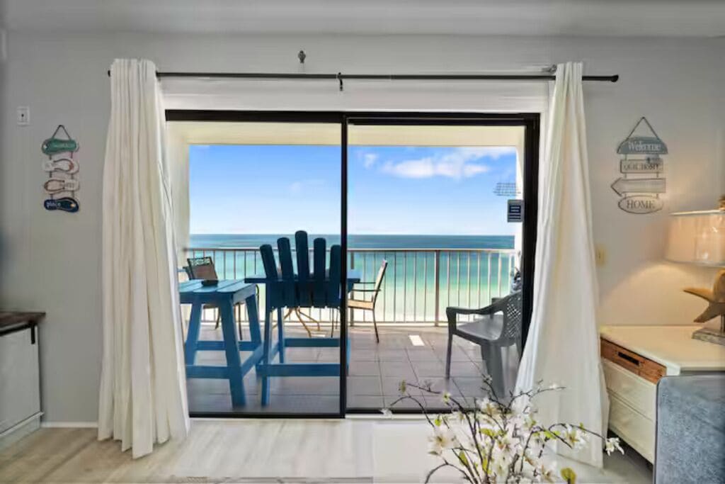 A room with a sliding glass door leading to a balcony with a view of the ocean.
