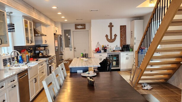 A modern kitchen with white cabinets, a wooden dining table, and a staircase. - Beachouse Direct Waterfront Private Beach (Milford)