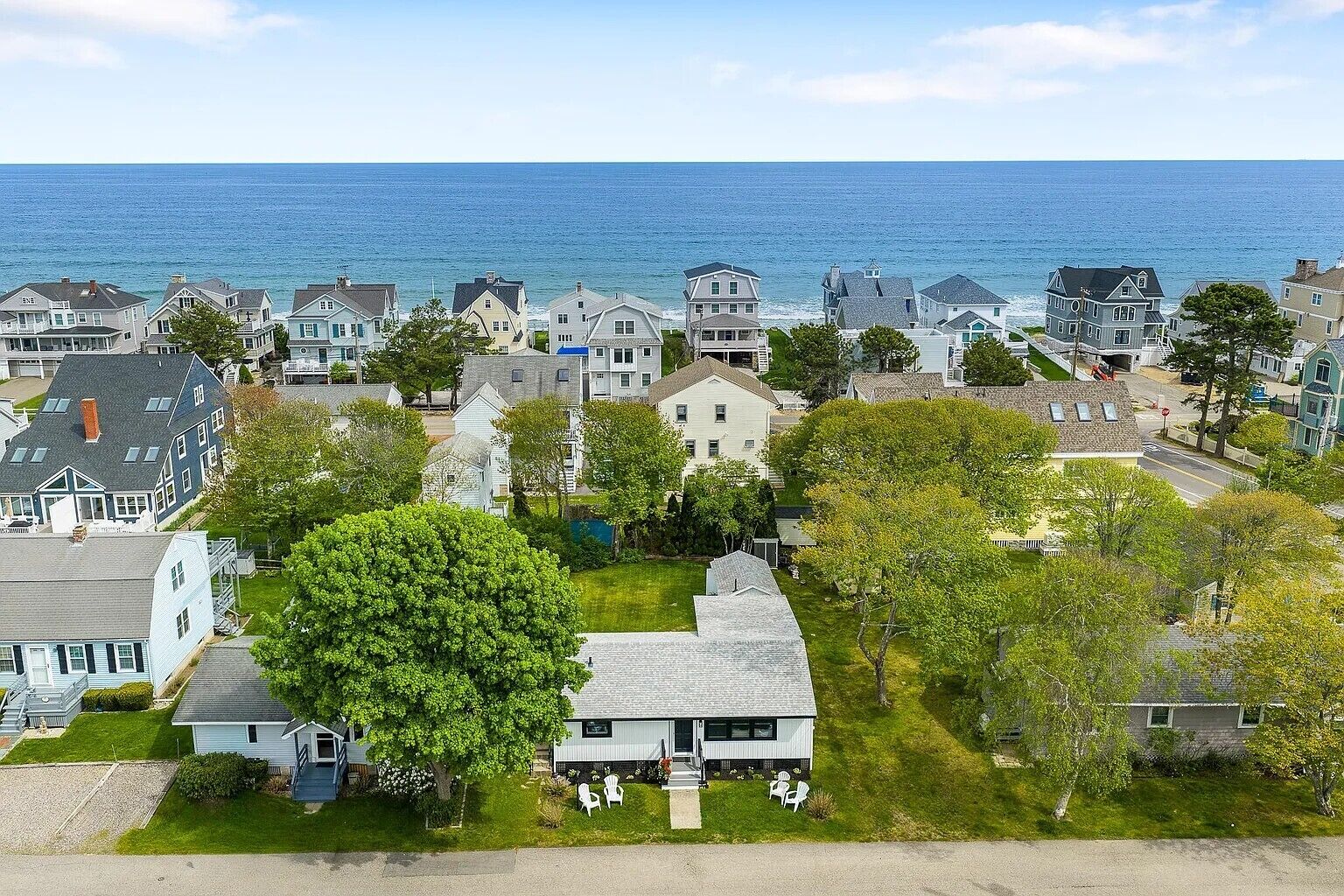 A coastal residential area with houses, a large tree, and a view of the ocean.