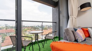 Un balcón con mesa y sillas, un sofá con cojines y vistas a edificios.