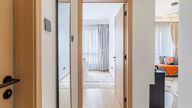Una habitación de hotel moderna con una puerta de madera, una cama con un rug colorido, un sofá con cojines y un escritorio con lámpara.