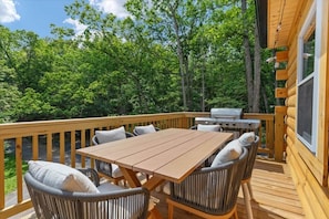 A wooden deck with a table and chairs, a grill, and a view of a forest. - Major's Retreat, Hot Tub, Sauna, Games, Near Bryce (Basye)