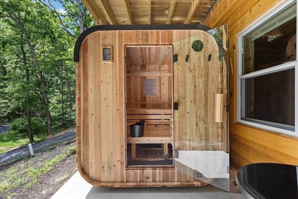 Une cabane en bois, dont la porte est ouverte, laissant entrevoir un petit intérieur avec un banc et un seau.