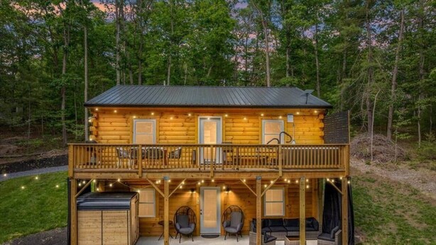 A two-story log cabin with a balcony, outdoor seating, and a deck with string lights.