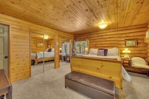 Ein Schlafzimmer in einer Blockhütte mit einem großen Bett, einer Bank, einem Spiegel und einem Fenster.