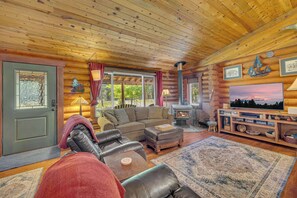 Ein Holzblockhaus-Interieur mit einer Couch, einem Hocker, einem Kamin, einem Fernseher und Holzwänden.