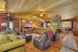 Ein Blockhaus-Interieur mit Kamin, Ledersessel, Holzregalen und einem Fernseher.