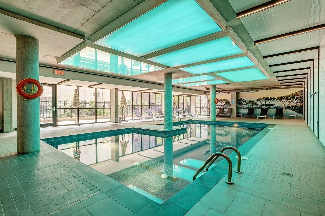 An indoor swimming pool with clear glass walls, a lifebuoy, and a view of the outside.