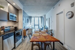Een moderne keuken met roestvrijstalen apparatuur, een eethoek met een houten tafel en geweven placemats, en een groot raam dat natuurlijk licht binnenlaat.