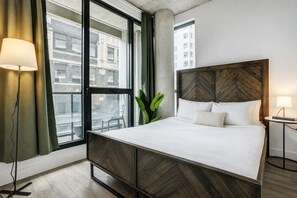 A hotel room with a large bed, a view of buildings through the window, and a small bedside table. - Montreal - C Lofts Le Smith 2 Bedroom (Montreal)